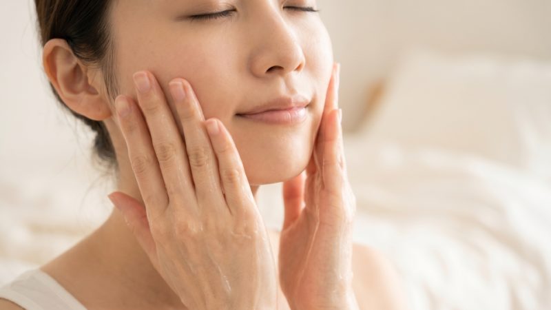 目を閉じ、両手のひらで顔全体を優しく包み込みながら、スキンケア成分を肌に馴染ませる女性。