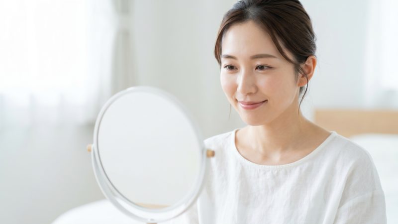 スキンケアの仕上げに鏡で肌の状態を確認する女性。オールインワンジェルで整った肌を見つめる様子。