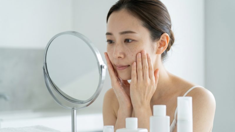 毎日のスキンケアでシミをケア。洗顔後、鏡を見ながら美白化粧品を顔全体になじませて保湿する女性。