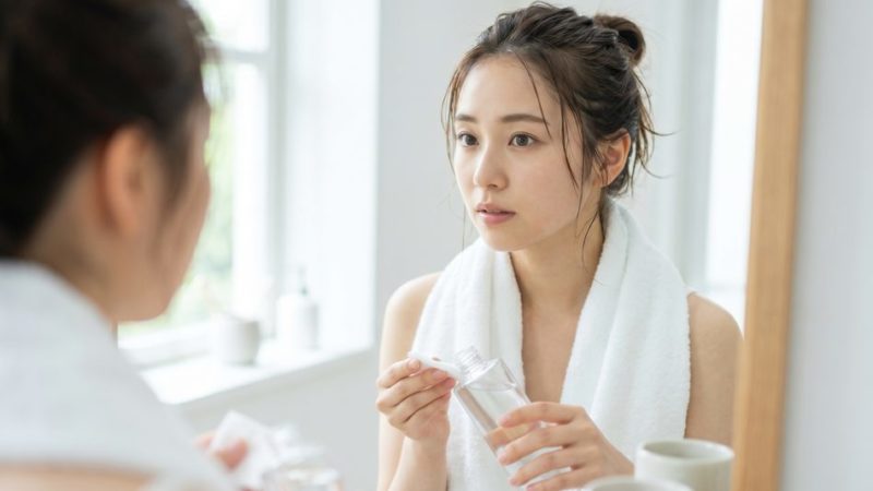 丁寧なスキンケアの第一歩として、洗面所で化粧水をコットンにたっぷりと染み込ませる女性。