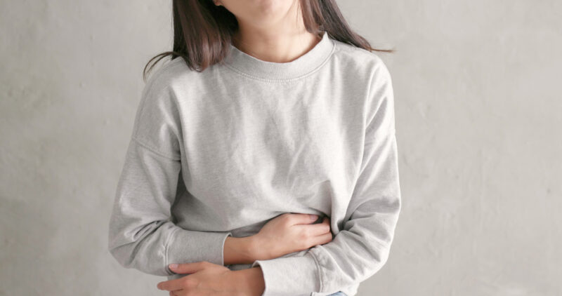 お腹の張りや痛み、便秘に悩む女性が、患部をさすりながら辛そうな表情を浮かべている様子。