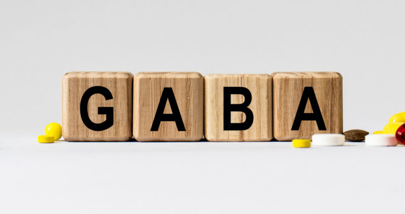 GABA（ギャバ）のアルファベットが書かれたウッドブロックと、健康維持やストレス緩和をイメージさせるサプリメントの錠剤。