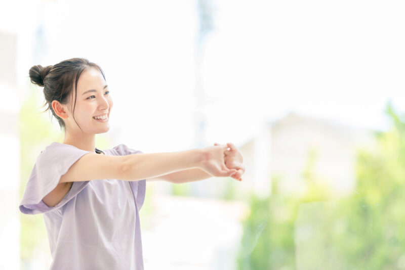 冷え性対策に効果的な血行を良くする方法として、屋外でリラックスしながらストレッチを楽しむ笑顔の女性。