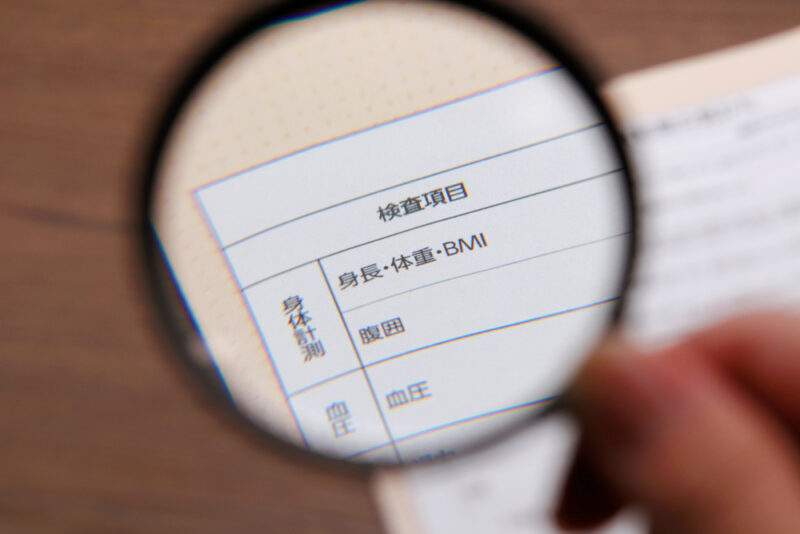 血圧の基本情報を確認するために、健康診断結果の血圧数値を虫眼鏡で詳しくチェックする様子。