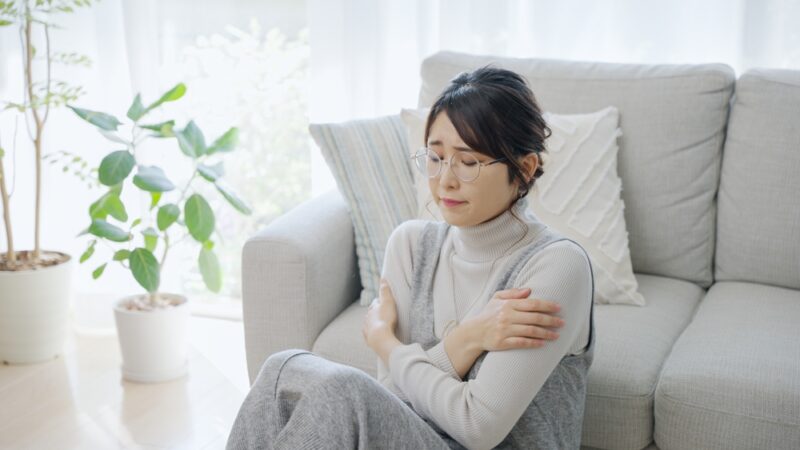 つらい冷え性の症状に悩み、部屋の中でも体温を逃がさないように肩を丸めて寒がる女性。