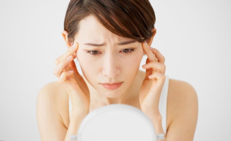 毛穴・乾燥対策のために肌を凝視する女性。セラミドサプリを導入する前に、鏡で現在の肌コンディションを詳細に把握しようとする場面。