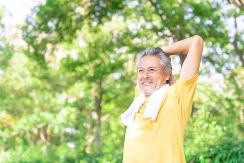 数値改善のために屋外で軽い運動を行い、健康的な笑顔を見せるアクティブシニアのストレッチ風景。
