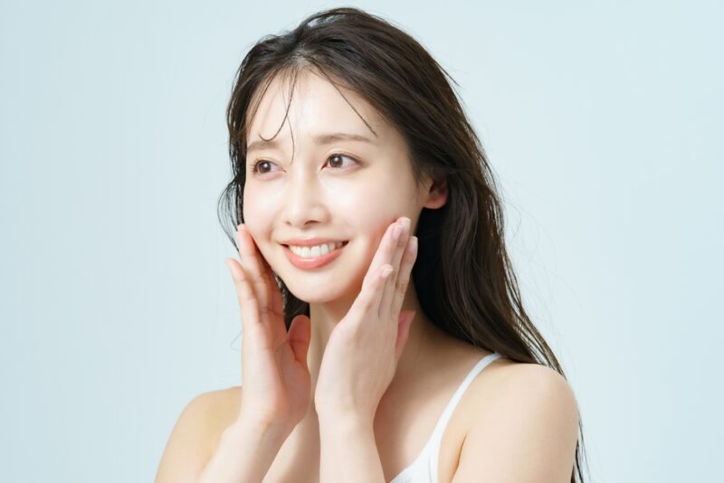 コラーゲンドリンクの口コミでも注目される肌のハリ。両手で優しく頬に触れ、晴れやかな笑顔を見せる女性。