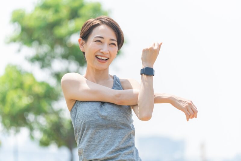 防風通聖散の効果を最大化するために、屋外で明るく前向きにストレッチ運動に取り組む女性。