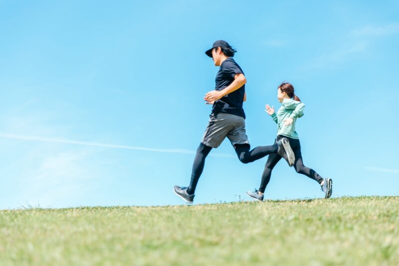 血糖値対策や脂肪減少をサポートする運動のイメージ。青空の下でランニングをする健康的な男女。