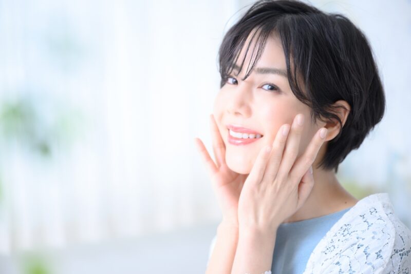 口コミで評判のコラーゲンドリンクで整った肌。頬を両手で触りながら、満足そうに微笑む透明感のある女性。