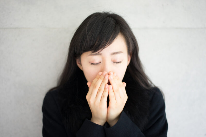 つらい冷え性の症状により、冬の寒さで冷え切った指先を自分の息で温めて血行を良くしようとする女性。
