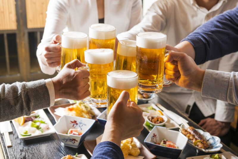 飲み会などの外食シーンでの尿酸値対策。大勢でビールジョッキを合わせて乾杯する賑やかな様子。