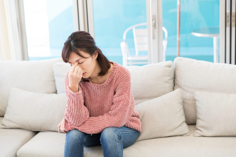 女性ホルモンの影響による自律神経の乱れから、頭痛や疲れを感じて目頭を押さえる女性。
