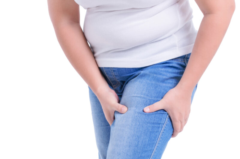 ダイエット中の女性がジーンズからはみ出るお腹周りや太ももの皮下脂肪を気にしている姿。