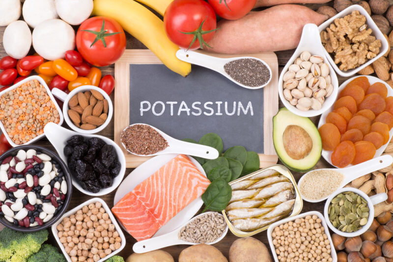 サーモンの切り身、トマト、バナナ、レンズ豆、ピスタチオが並び、中央にPOTASSIUMと書かれた小さな黒板。