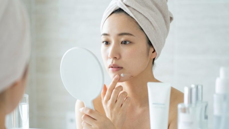 お風呂上がりの清潔な肌に、顎周りのニキビや肌荒れを改善するための薬用クリームをピンポイントで塗る女性。