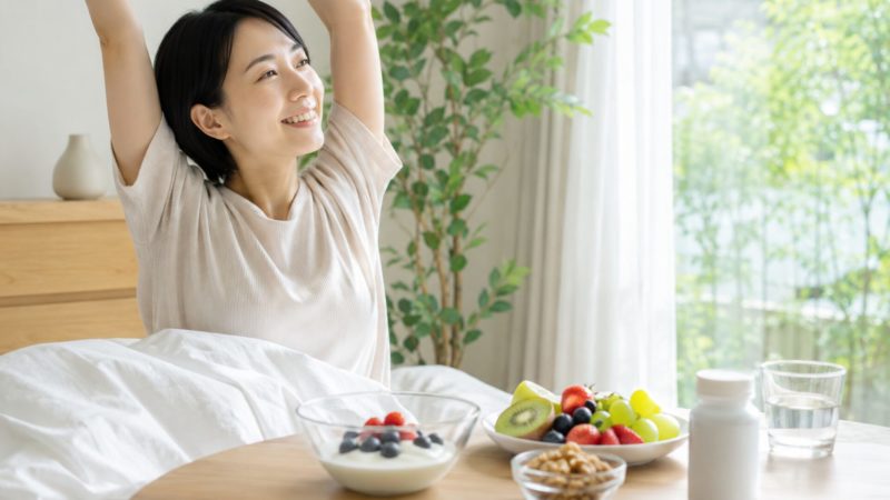 乳酸菌サプリやヨーグルトなどの朝食を摂り、健康的な毎日を過ごして晴れやかに目覚める女性。
