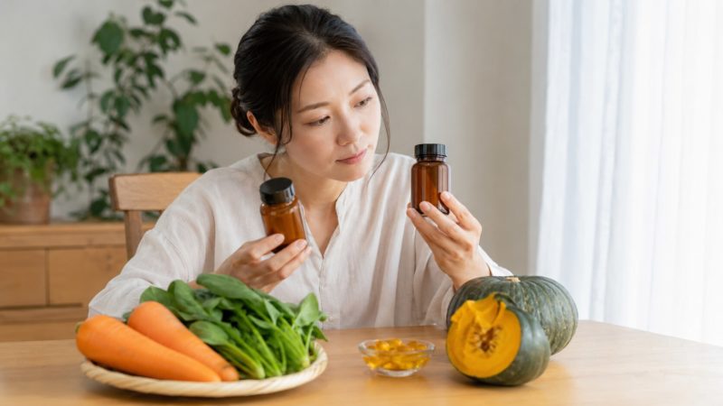 サプリメントのラベルを確認して比較する女性。ビタミンAを食品とサプリの両面から賢く選ぶためのQ&Aイメージ。