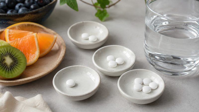 自分に合ったビタミンCサプリの選び方をイメージし、数種類の錠剤と新鮮な果物、水の入ったグラスを並べた比較風景。