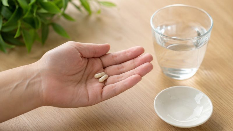手軽に摂取できる形状のオルニチンサプリ。カプセル2粒を手のひらに乗せ、水で飲む準備をしている場面。