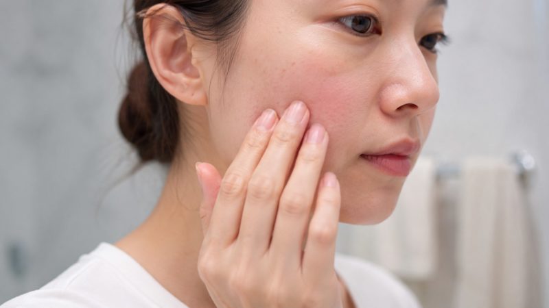 シミの原因を知るために、自分の肌を指で触りながらシミの状態をチェックする女性の横顔。