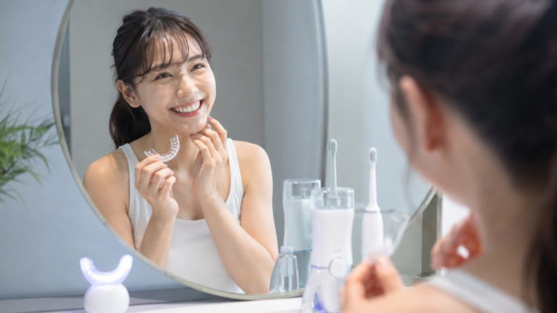 マウスピース矯正の治療効果を鏡で確認し、満足そうに微笑む女性。清潔感のある洗面所での一コマ。