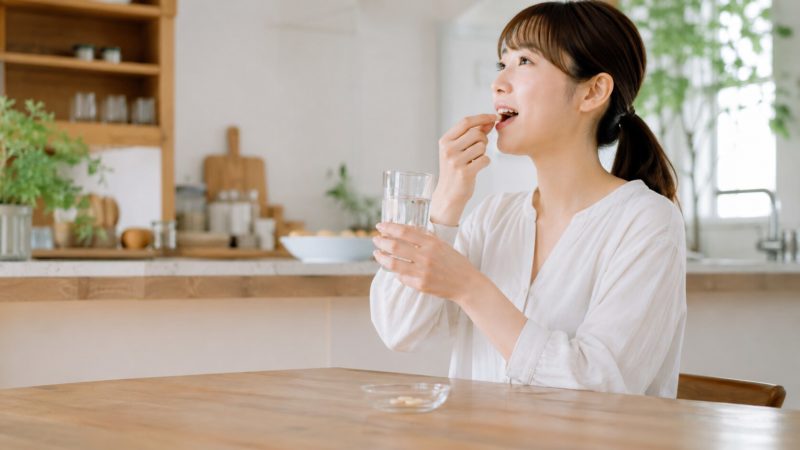 ビタミンAサプリを正しく摂取する様子。適切な単位や目安量を意識しながら、水と一緒に飲む女性の横顔。