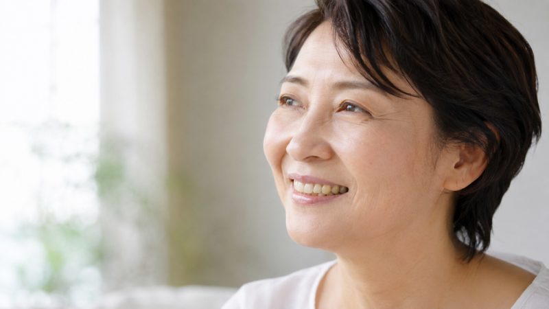 優しく微笑むショートヘアの女性。口元からは少し黄みを帯びた自然な色の歯が見えている。
