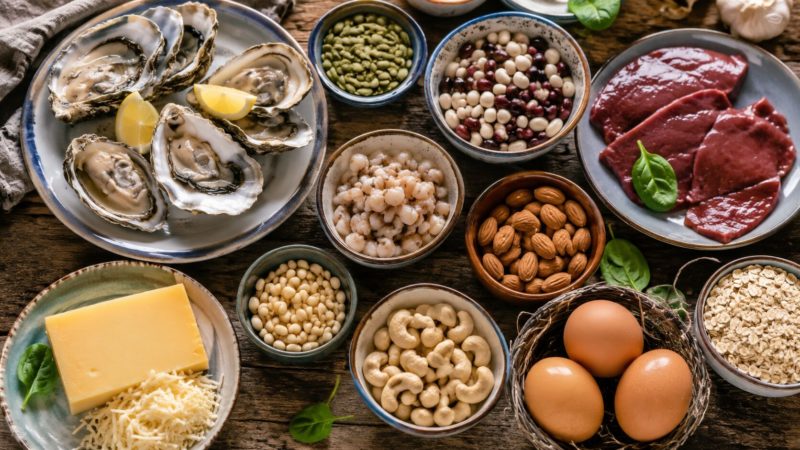 皿に盛られた生牡蠣、レバー、卵、カシューナッツ、チーズ、大豆などが並ぶ、木目調のテーブル。