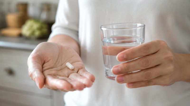 おすすめの亜鉛サプリの飲み方を解説。手のひらに準備した白いカプセルとコップ一杯の水。