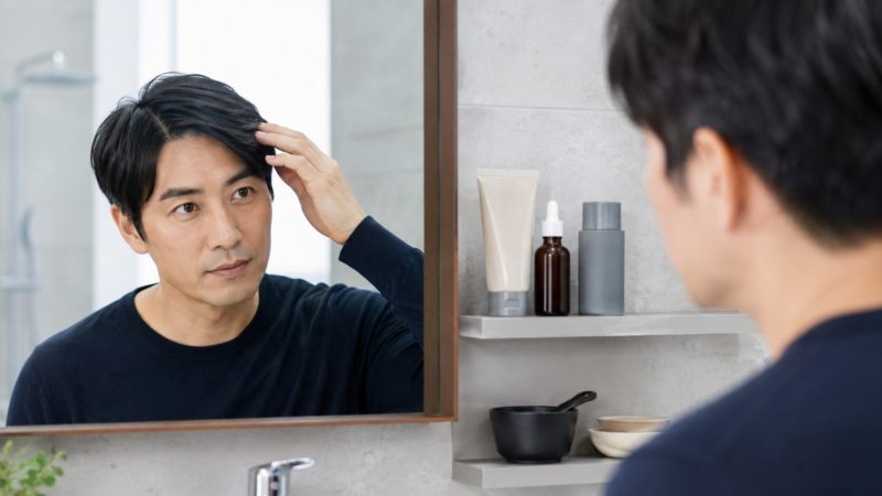 白髪ケアと薄毛対策を両立する際のポイント。育毛剤と白髪染めを併用する際に気になる頭皮の状態を確認する男性。