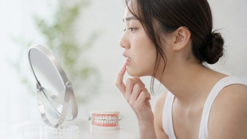 マウスピース矯正を検討中の女性が、鏡を見ながら自分の前歯の歯並びや噛み合わせを確認する様子。