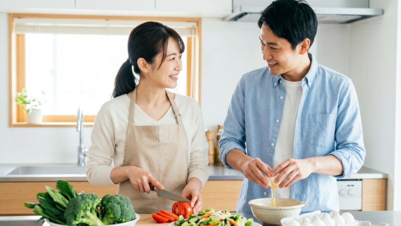 夫婦で一緒に妊活中の食事を準備する様子。ブロッコリーなどの野菜を切りながら談笑する二人。