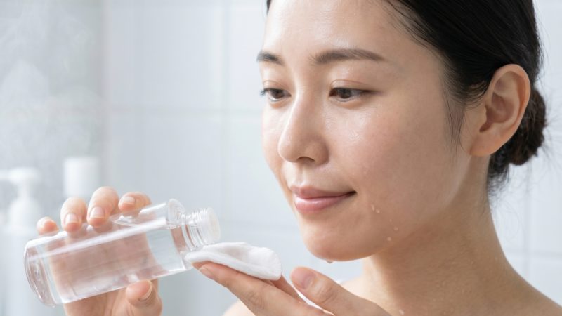 毛穴ケア化粧水の使い方を実践する女性。透明なボトルからコットンにたっぷりとローションを染み込ませるスキンケアの様子。